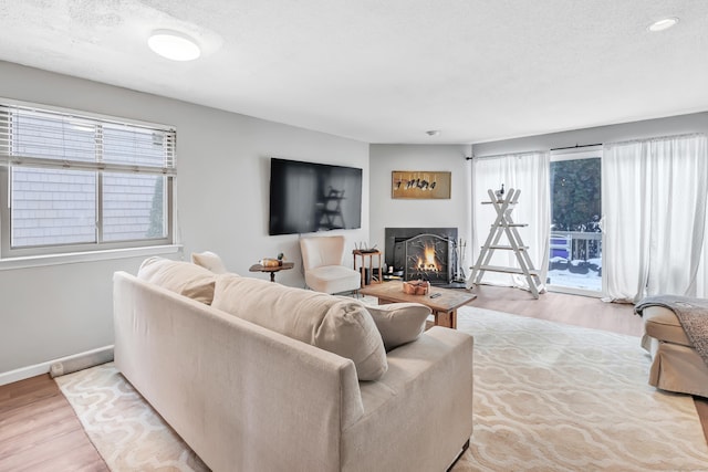 living room featuring a lit fireplace, a textured ceiling, baseboards, and wood finished floors