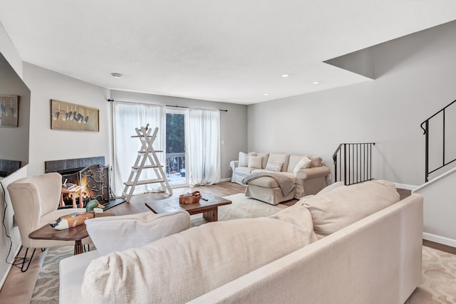 living area featuring recessed lighting, light wood-type flooring, a lit fireplace, baseboards, and stairs