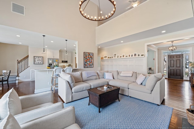 living room featuring dark wood-type flooring, a towering ceiling, visible vents, stairway, and crown molding