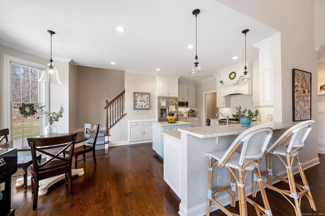 kitchen featuring dark wood-style flooring, a peninsula, stainless steel appliances, white cabinetry, and pendant lighting