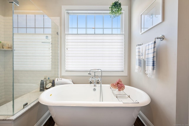 full bath with a soaking tub, a healthy amount of sunlight, and baseboards