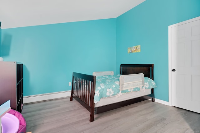 bedroom with a baseboard heating unit, baseboards, and wood finished floors