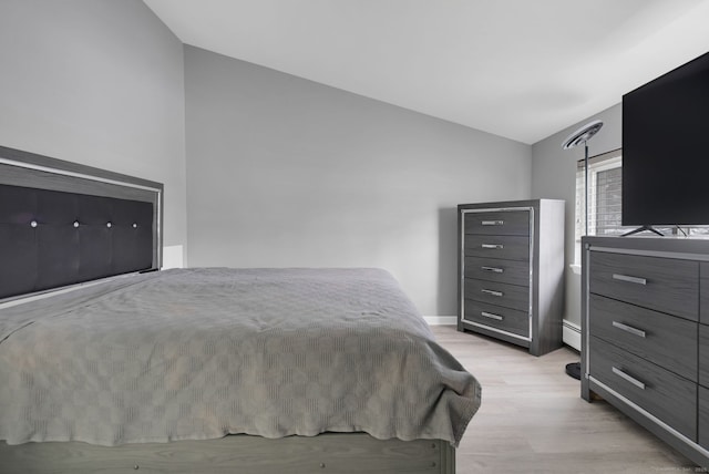 bedroom featuring vaulted ceiling, a baseboard heating unit, light wood finished floors, and baseboards