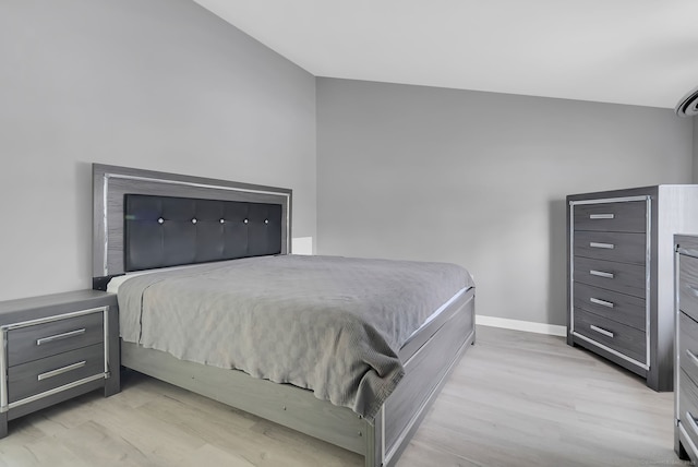 bedroom with light wood-type flooring, vaulted ceiling, and baseboards