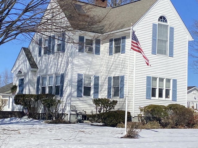 snow covered property featuring a chimney and roof with shingles