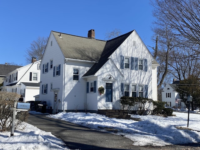 view of front facade with roof with shingles and a chimney