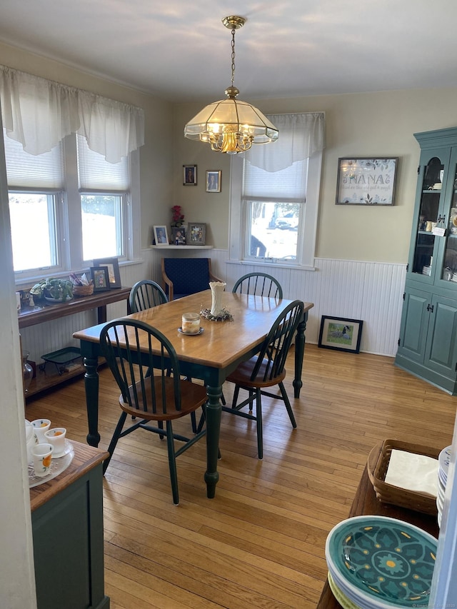 dining area with a wainscoted wall, light wood-style flooring, and a notable chandelier