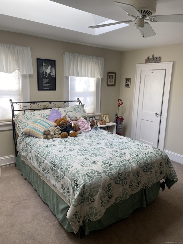 bedroom featuring a skylight, light carpet, baseboards, and multiple windows