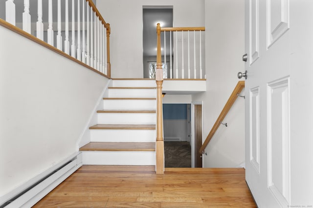 stairs featuring a high ceiling, baseboard heating, and wood finished floors