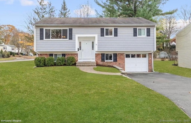 raised ranch featuring driveway, brick siding, a front lawn, and an attached garage