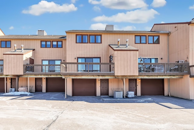 back of property featuring an attached garage, cooling unit, a balcony, driveway, and a chimney