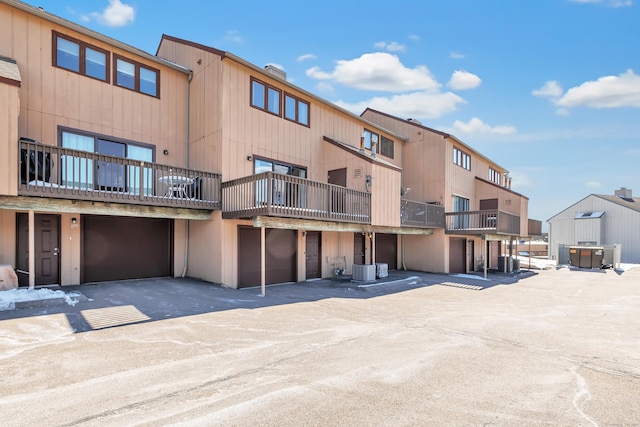 view of building exterior featuring central AC, driveway, an attached garage, and a residential view