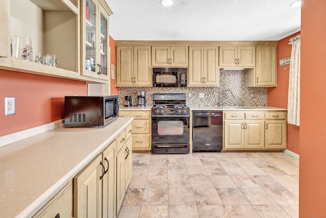 kitchen with glass insert cabinets, a sink, light countertops, black appliances, and backsplash