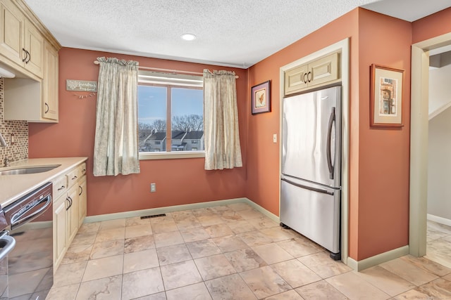 kitchen featuring black dishwasher, cream cabinetry, light countertops, freestanding refrigerator, and a sink