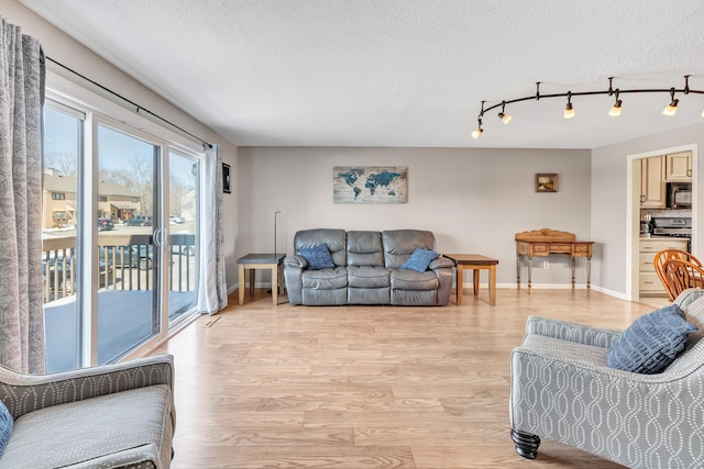 living room with a textured ceiling, rail lighting, light wood-style flooring, and baseboards