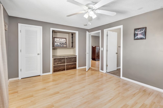 unfurnished bedroom with light wood-type flooring, ceiling fan, a textured ceiling, and baseboards