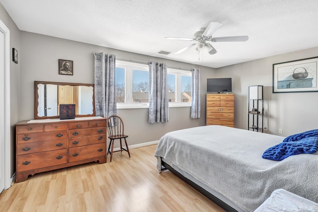 bedroom with baseboards, visible vents, a ceiling fan, a textured ceiling, and light wood-type flooring