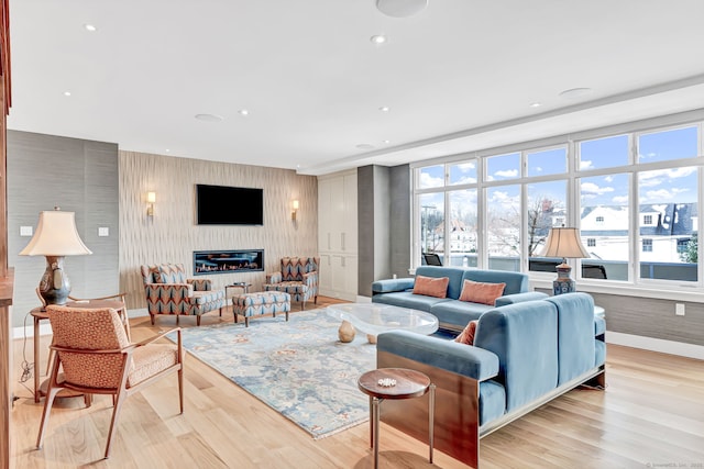 living room with recessed lighting, baseboards, a glass covered fireplace, and light wood finished floors