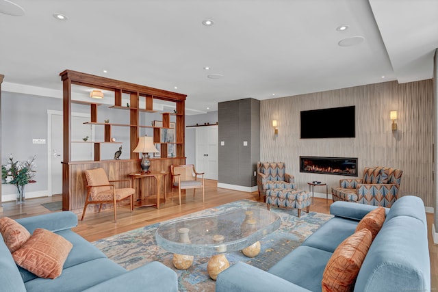 living room featuring a barn door, baseboards, a glass covered fireplace, wood finished floors, and recessed lighting