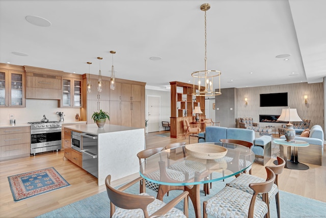 dining space featuring light wood finished floors, a lit fireplace, a notable chandelier, and recessed lighting