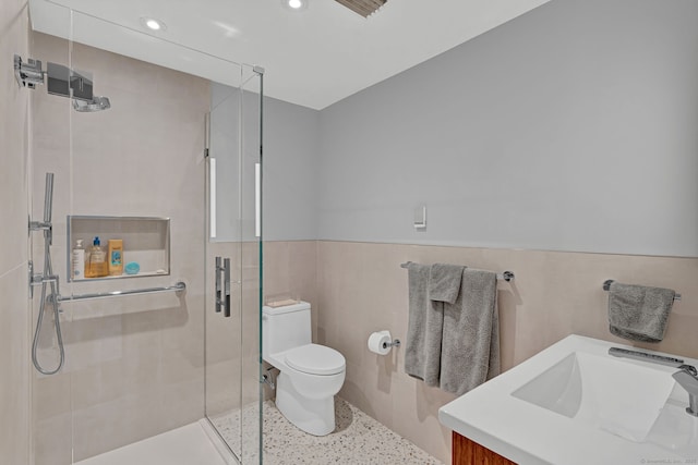 full bathroom with a wainscoted wall, tile walls, toilet, a shower stall, and vanity