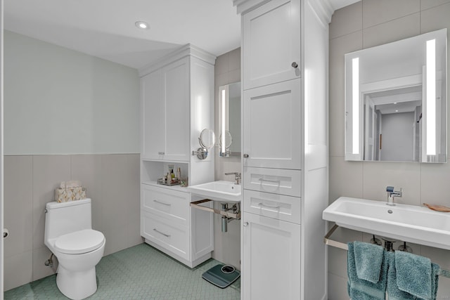 bathroom featuring toilet, a sink, tile patterned flooring, and tile walls