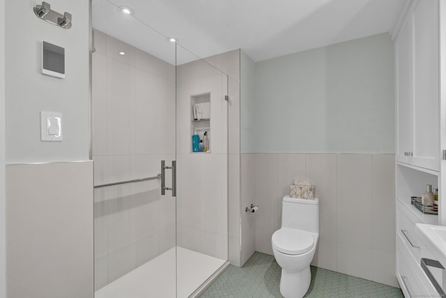 full bathroom featuring tile patterned flooring, toilet, a wainscoted wall, tile walls, and a stall shower