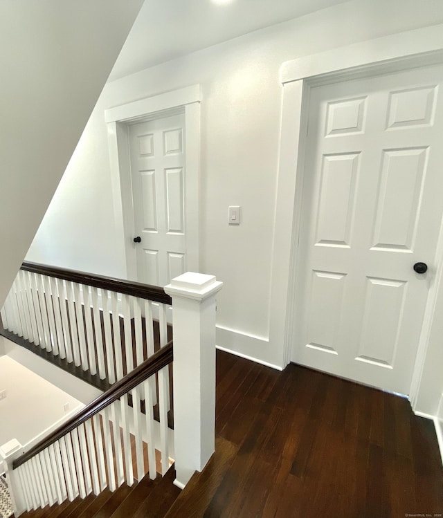 corridor with baseboards, an upstairs landing, and dark wood-type flooring