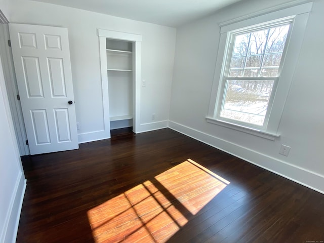 unfurnished bedroom featuring baseboards, multiple windows, and dark wood-type flooring