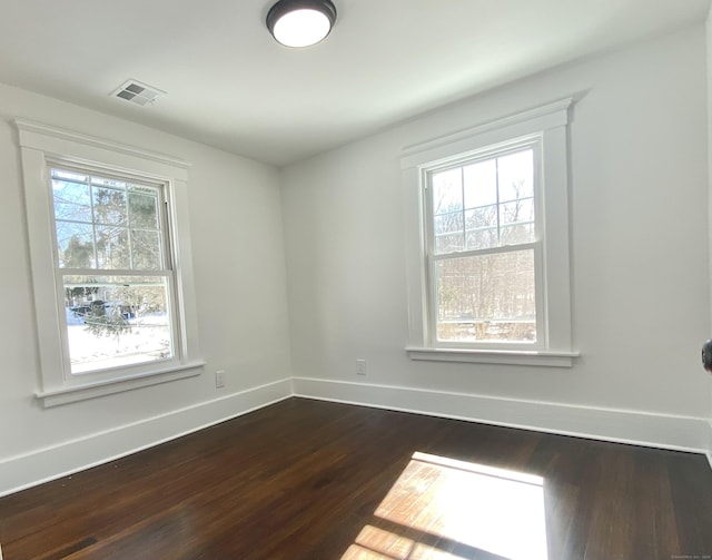 empty room with baseboards, visible vents, and dark wood-type flooring