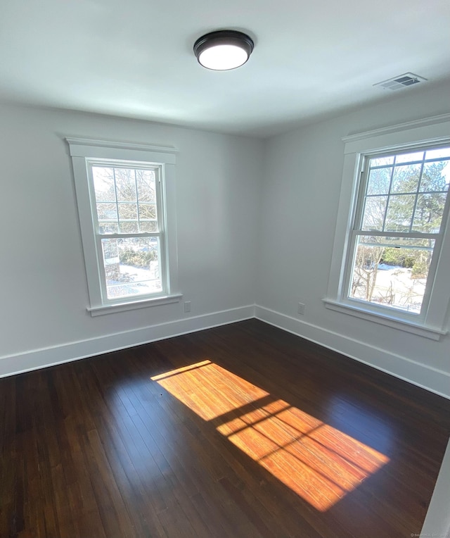 unfurnished room with baseboards, visible vents, dark wood-style floors, and a healthy amount of sunlight