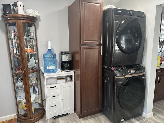 washroom with stacked washer and dryer, light wood-style flooring, and cabinet space