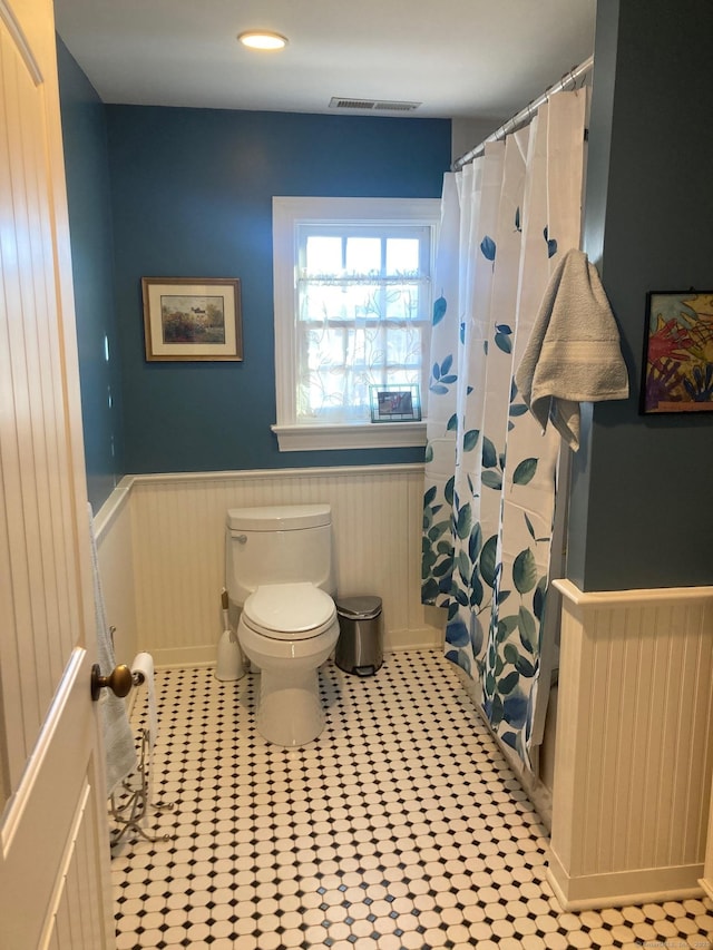 bathroom with a shower with shower curtain, wainscoting, visible vents, and toilet