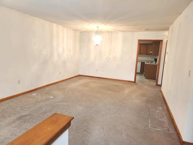 empty room featuring an inviting chandelier, baseboards, and light colored carpet