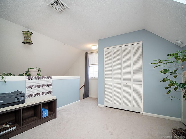 interior space featuring visible vents, vaulted ceiling, a textured ceiling, and light colored carpet