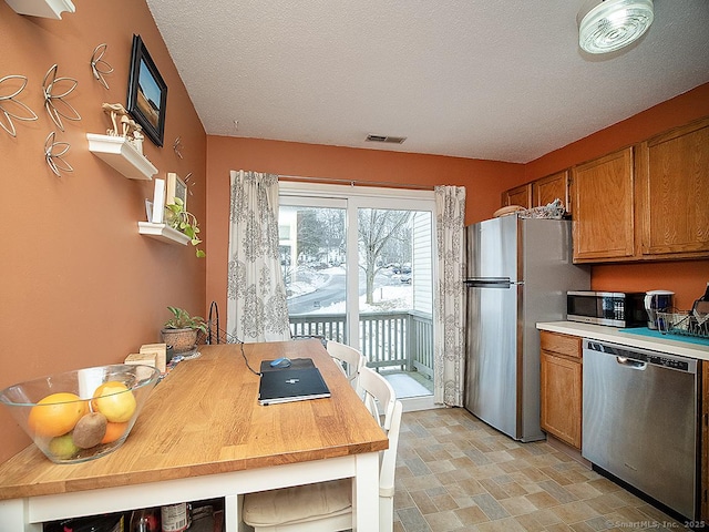 kitchen featuring stainless steel appliances, brown cabinetry, light countertops, and visible vents