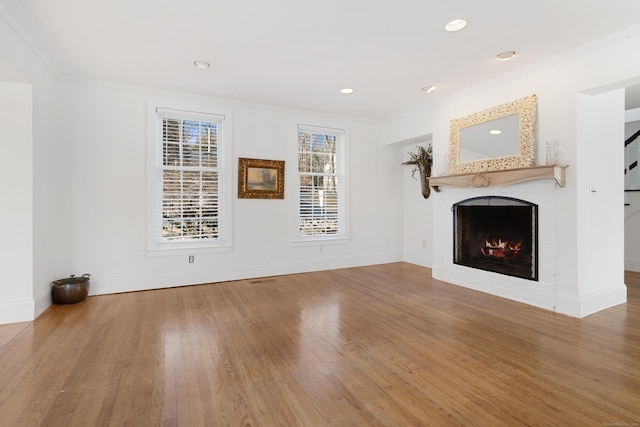 unfurnished living room featuring a warm lit fireplace, baseboards, wood finished floors, crown molding, and recessed lighting