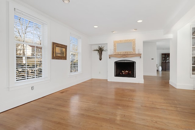 unfurnished living room featuring a lit fireplace, ornamental molding, recessed lighting, and light wood-style floors