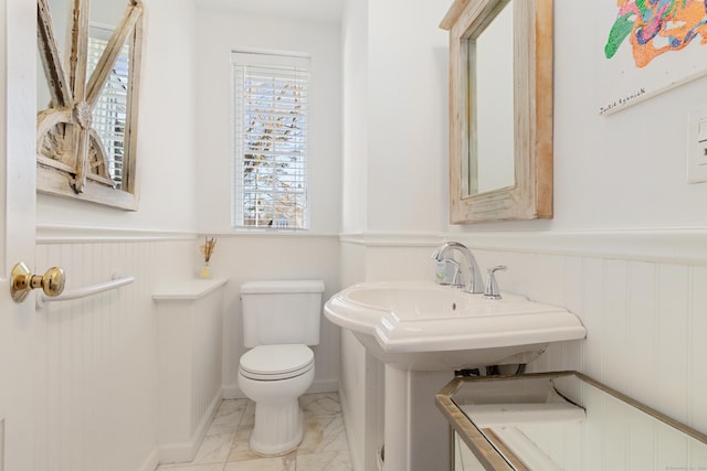 half bath with toilet, a wainscoted wall, and marble finish floor