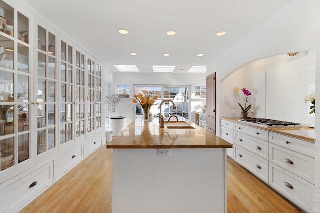 kitchen featuring dark stone counters, a sink, light wood-style flooring, and stainless steel gas stovetop