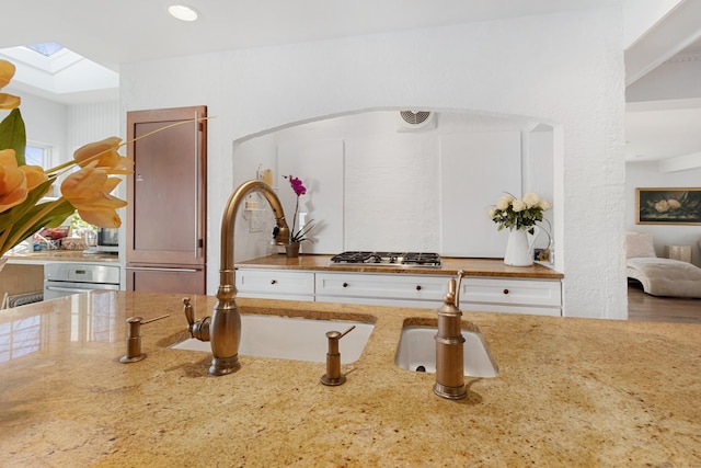 details featuring light stone countertops, stainless steel gas stovetop, a skylight, and a sink