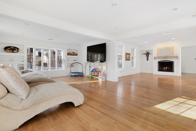 living room with built in features, recessed lighting, a warm lit fireplace, and light wood-style floors