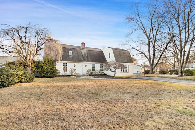 view of front of home featuring a front lawn, roof with shingles, a chimney, and a gambrel roof