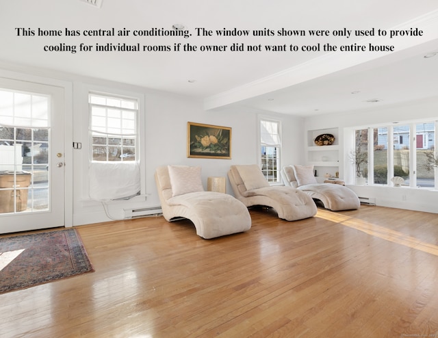 sitting room with built in shelves, baseboard heating, hardwood / wood-style flooring, and a healthy amount of sunlight