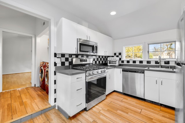 kitchen featuring white cabinets, dark countertops, independent washer and dryer, stainless steel appliances, and a sink