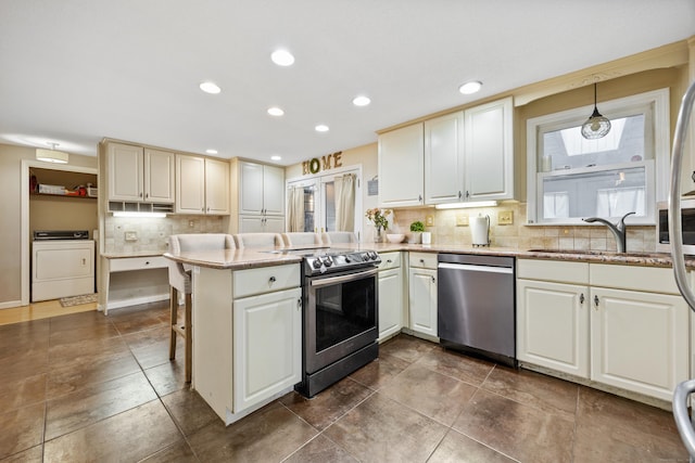 kitchen with washer / dryer, a peninsula, a sink, appliances with stainless steel finishes, and tasteful backsplash