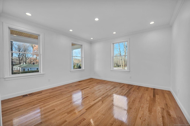 empty room featuring baseboards, light wood-style flooring, visible vents, and crown molding