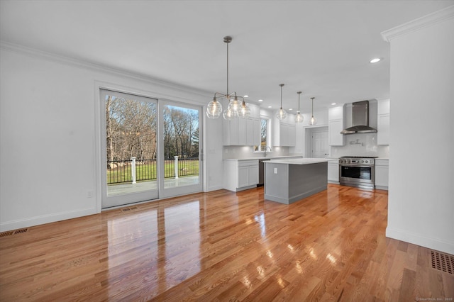 kitchen featuring stainless steel appliances, light countertops, hanging light fixtures, white cabinets, and wall chimney exhaust hood