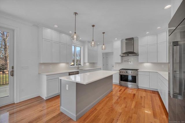 kitchen featuring light countertops, white cabinetry, a sink, wall chimney range hood, and high quality appliances