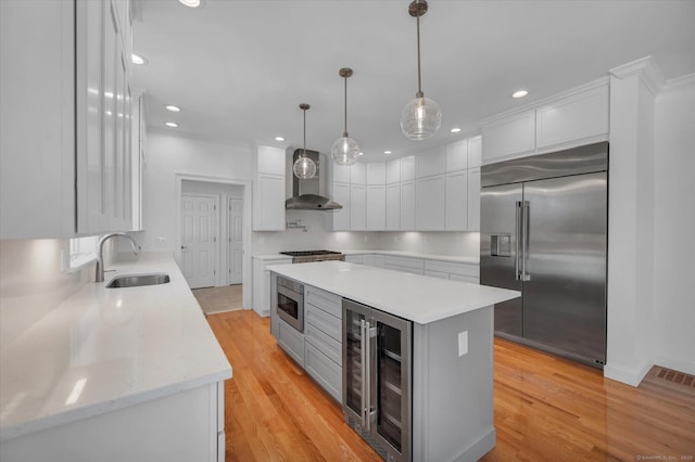 kitchen with beverage cooler, built in appliances, white cabinetry, pendant lighting, and a sink